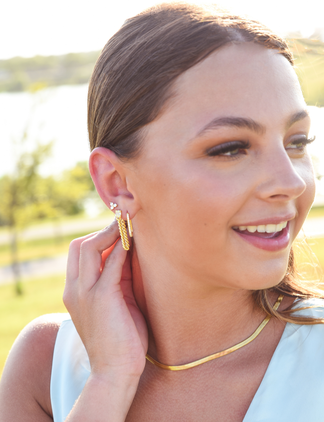 Burdlife model displaying 3 earrings including the Luxe Oval Hoops, the Refined Single Chain Earring and the Modish Triple Crystal Studs. 