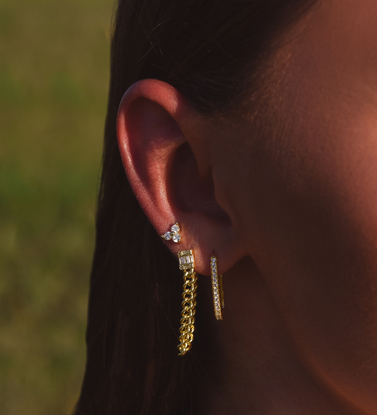 Side of Burdlife Model's head displaying 3 earrings including the Luxe Oval Hoops, the Refined Single Chain Earring and the Modish Triple Crystal Studs. 