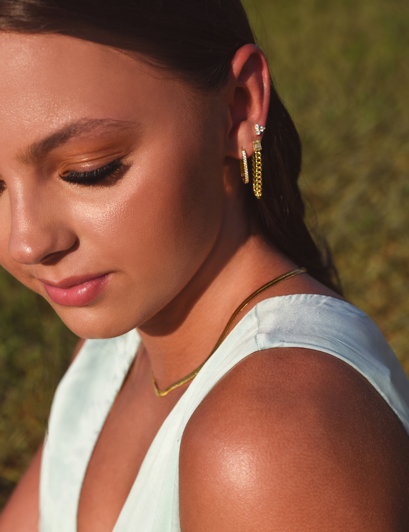 Side of Burdlife Model's head displaying 3 earrings including the Luxe Oval Hoops, the Refined Single Chain Earring and the Modish Triple Crystal Studs. 