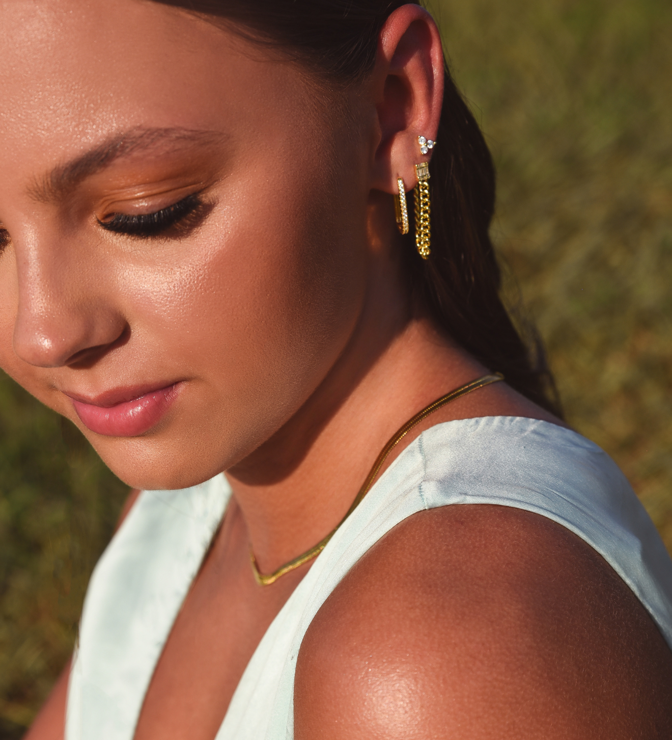 Side of Burdlife Model's head displaying 3 earrings including the Luxe Oval Hoops, the Refined Single Chain Earring and the Modish Triple Crystal Studs. 